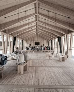 people are sitting at tables in the middle of a large room with wooden floors and beams