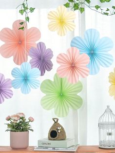 colorful paper fans hanging from the ceiling above a table with flowers and books on it