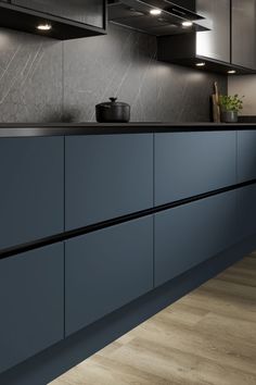 a kitchen with dark blue cabinets and black counter tops, along with wooden flooring