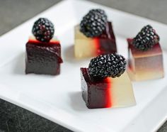 four desserts on a white plate topped with blackberries and raspberry sauce