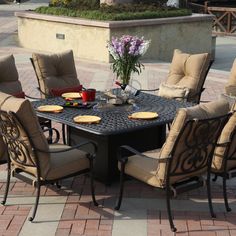 an outdoor dining table and chairs set up on a brick patio in front of a fountain