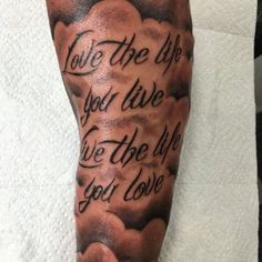 a man's arm with an ink quote on it and clouds in the background