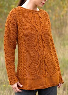 a woman wearing an orange sweater standing in the grass