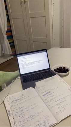 an open laptop computer sitting on top of a white table next to a bowl of cherries