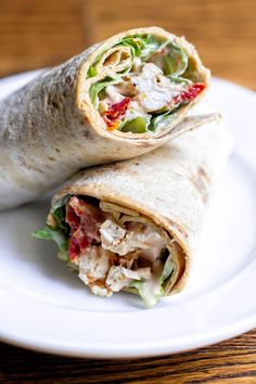 a burrito with chicken, lettuce and tomatoes on it sitting on a plate