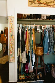 an open closet with clothes and shoes hanging on the rack, in front of a painting