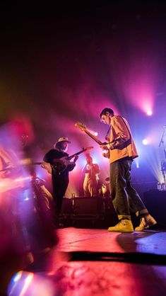 two men standing on stage with guitars in front of purple and red lights behind them