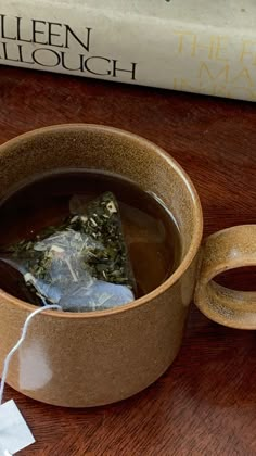 a cup of tea next to a book on a wooden table with a white tag