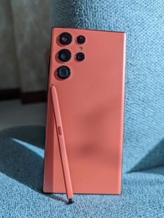 an orange cell phone sitting on top of a blue couch next to a pink pen