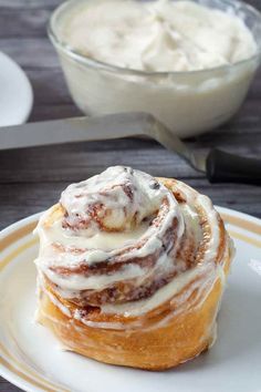 a cinnamon roll sitting on top of a white plate next to a bowl of cream