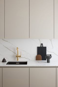 a white kitchen with marble counter tops and gold faucet on the side wall