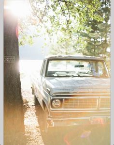 an old car is parked next to a tree in the woods with sunlight streaming through it