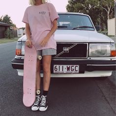 a woman holding a skateboard standing in front of a car