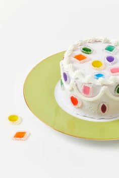 a white cake with multicolored icing on a green plate next to small candies