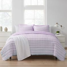 a bed with purple and white bedspread in front of a window on a wooden floor