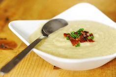 a white bowl filled with soup on top of a wooden table next to a spoon