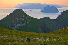 a person is walking in the grass with mountains in the background and water on the other side