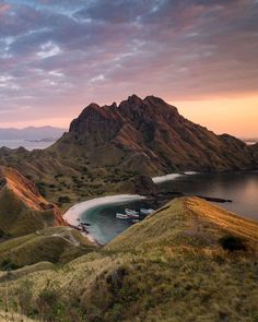 boats are docked in the water at sunset on an island with green hills and grass