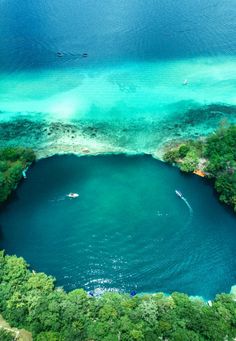 an aerial view of a lake surrounded by trees and blue water with boats in it