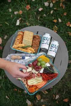 a person holding a tray full of food on top of a table with two cans of beer