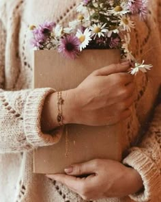 a woman holding a brown box with flowers in it's hands and wearing bracelets