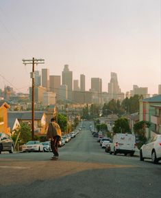 a man riding a skateboard down the middle of a street next to parked cars