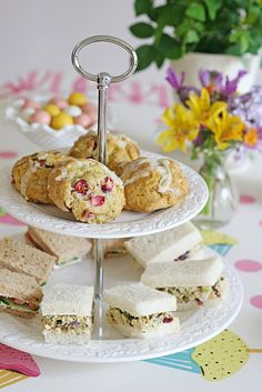 three tiered plate with sandwiches and muffins on it, next to flowers