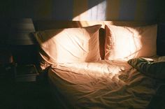 an unmade bed with two pillows on it in a dark room next to a lamp