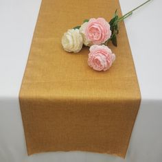 three pink and white flowers are on top of a brown table cloth that has been draped over it