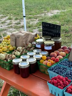 various fruits and jams are on display at an outdoor market table in the grass