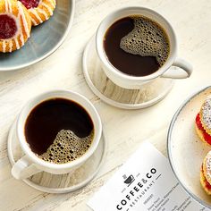 two cups of coffee sit next to pastries on a plate and paper that says coffee & co