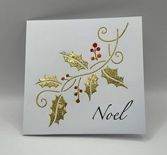 a white card with gold foiling and holly leaves on it, which reads noel