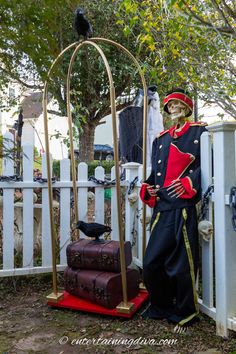 a skeleton dressed up as a soldier next to suitcases in front of a white picket fence