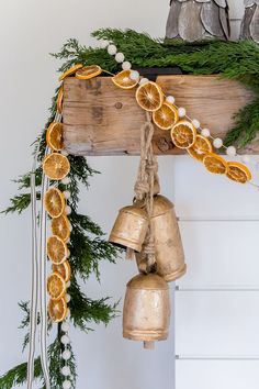 two bells with orange slices on them hanging from a wooden beam decorated with garland and pine cones