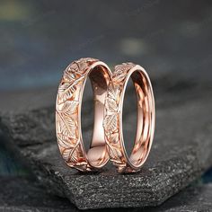 two rose gold wedding rings sitting on top of a rock next to another ring that is engraved with leaves