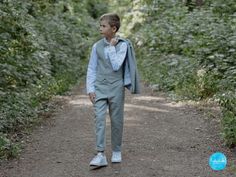 a young boy in a suit walking down a dirt road