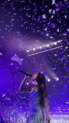 a woman singing into a microphone on stage with confetti falling from the ceiling