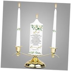 two white candles are on a gold plated stand with a card in the middle