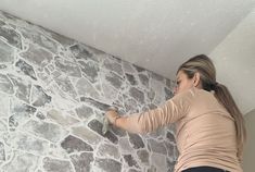 a woman painting a stone wall with paint rollers