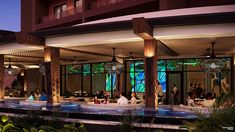 people are sitting at tables in front of a building with large glass windows and palm trees