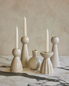 three candles are sitting next to each other on a marble table with two vases and one candle holder