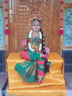 a woman sitting on top of a golden bench wearing a green and pink outfit with beads