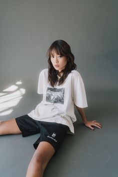 a woman sitting on the ground with her legs crossed wearing shorts and a t - shirt