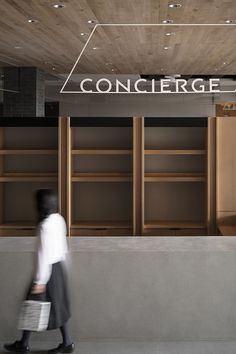 a woman walking past a book shelf filled with lots of wooden shelves and shelving