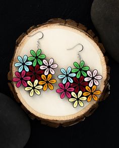 the colorful flower earrings are on display next to a piece of wood and black stones