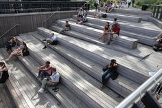 many people are sitting and walking on the wooden steps in an open area with metal railings