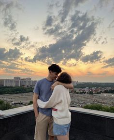 a man and woman standing on top of a building with the sun setting in the background