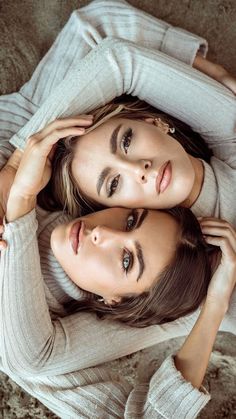 two beautiful young women laying on the floor posing for a photo in their sweaters