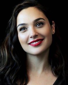 a woman with long dark hair and red lipstick smiling at the camera, wearing a black top