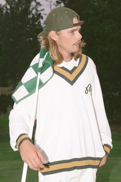 a young man holding a baseball bat on top of a green and white field with trees in the background